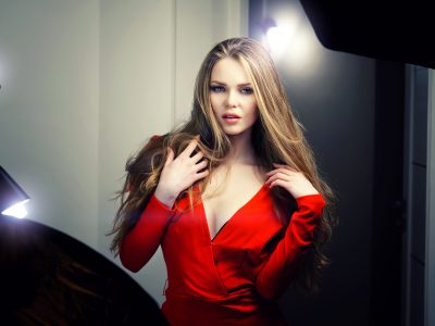 Beautiful sexy young caucasian woman in red dress and deep blue eyes looking straight into the camera. Backstage dramatic studio shot.