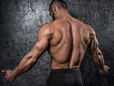 Man showing his muscular back against conctete wall