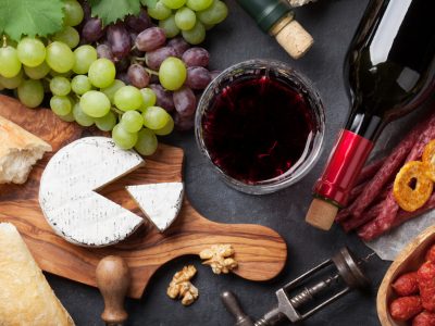 Red and white wine, grape, cheese and sausages over stone table. Top view