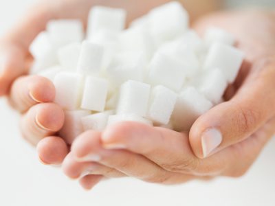 food, junk-food, diabetes and unhealthy eating concept - close up of white lump sugar in woman hands