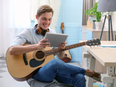 Young man with guitar and tablet sitting at table